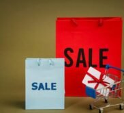 Bright sale bags with a gift in a shopping cart against a neutral background.