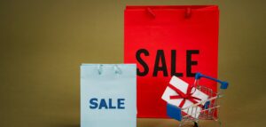 Bright sale bags with a gift in a shopping cart against a neutral background.
